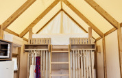 Safari tent interior with wooden bunk beds, ladder, fridge and a woven light fixture hanging from the ceiling.