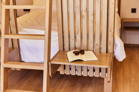 Interior de tienda safari con litera de madera, mesa, libro abierto y gafas de sol, ambiente acogedor.