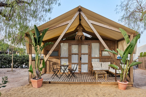 Safari-inspiriertes Glamping-Zelt Alhamilla mit Holzveranda, Sitzbereich und tropischen Pflanzen davor.