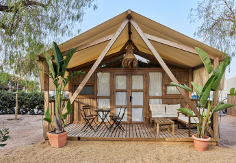 Tenda da glamping stile safari Alhamilla con veranda in legno, area relax e palme in vaso all'ingresso.