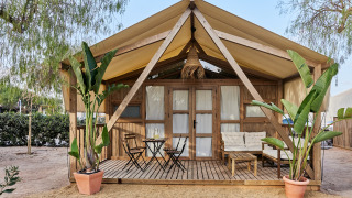 Safari-inspiriertes Glamping-Zelt Alhamilla mit Holzveranda, Sitzbereich und tropischen Pflanzen davor.