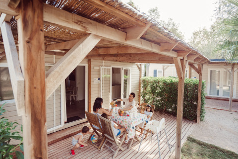 Gezin aan het ontbijt op het houten terras van Bungalow Confort Baconé, omgeven door groen.