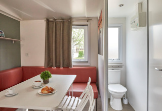 Vista interior del Bungalow Confort Baconé en TAIGA Delta de l'Ebre con zona de comedor y baño visible.