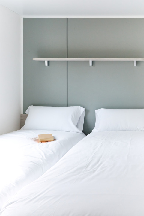 Zwei Einzelbetten mit weißen Bettlaken im Bungalow Confort Baconé, TAIGA Delta de l'Ebre, Spanien.