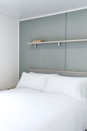 Dormitorio con cama grande de sábanas blancas y estante, en Bungalow Confort Baconé, TAIGA Delta de l'Ebre, España.