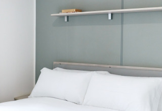 Schlafzimmer mit Doppelbett und weißer Bettwäsche, Regal darüber in der Bungalow Confort Baconé, TAIGA Delta de l'Ebre.