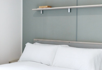 Chambre avec grand lit blanc et étagère, photo prise à Bungalow Confort Baconé, TAIGA Delta de l'Ebre, Espagne.