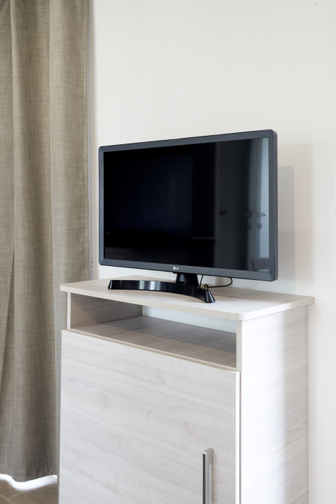 Televisor de pantalla plana sobre mueble de madera clara junto a cortina beige en Bungalow Confort Baconé, TAIGA Delta de l'Ebre.