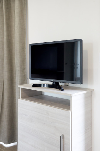 Televisor de pantalla plana sobre mueble de madera clara junto a cortina beige en Bungalow Confort Baconé, TAIGA Delta de l'Ebre.