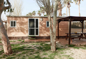 Wooden cabin named Bungalow Essential Banya with covered terrace, picnic bench, and grassy outdoor area