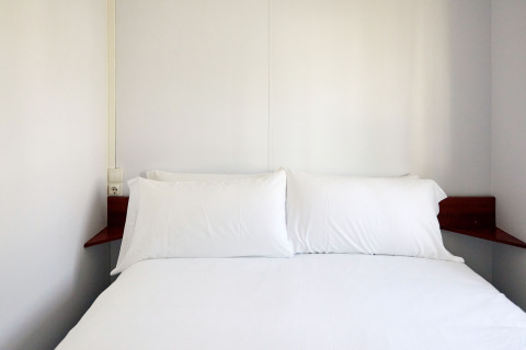 Dormitorio minimalista en Bungalow Essential Golero, TAIGA Delta de l'Ebre, España, con ropa de cama blanca.