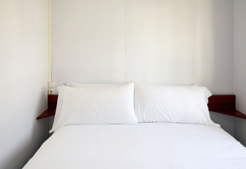 Dormitorio minimalista en Bungalow Essential Golero, TAIGA Delta de l'Ebre, España, con ropa de cama blanca.