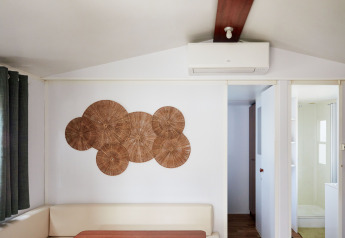 Wohnbereich im Bungalow Essential Golero bei TAIGA Delta de l'Ebre, Spanien, mit Wandkunst und Klimaanlage.