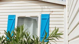 Cabaña blanca con contraventanas azules y vegetación en primer plano, vista en Bungalow Confort Delta.