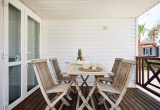 Terraza exterior de madera en Bungalow Confort Delta con mesa, sillas y piña como centro de mesa.