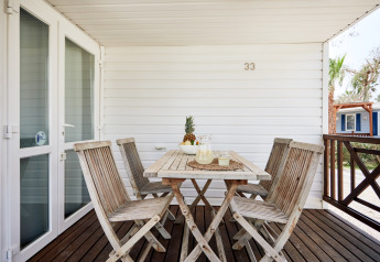 Terraza exterior de madera en Bungalow Confort Delta con mesa, sillas y piña como centro de mesa.