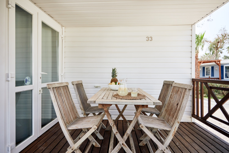 Terraza exterior de madera en Bungalow Confort Delta con mesa, sillas y piña como centro de mesa.