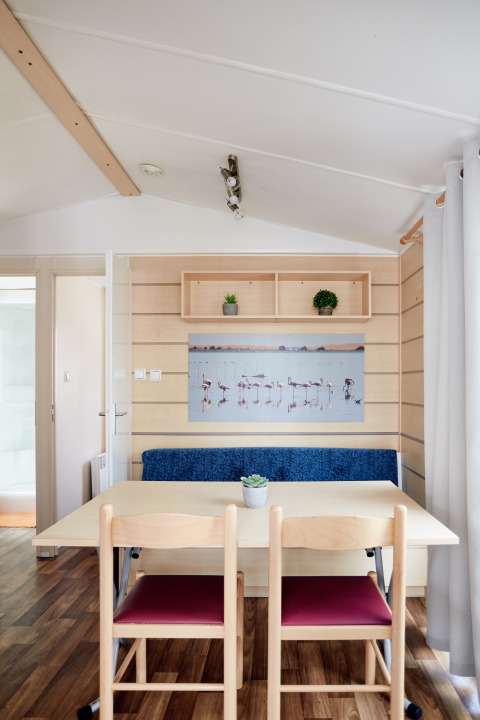 Interiør af Bungalow Confort Delta med spisebord, to stole, blå bænk og vægkunst med flamingoer.