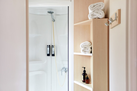Modern shower area with white towels, wooden shelves, and dispensers at Bungalow Confort Delta cabin.