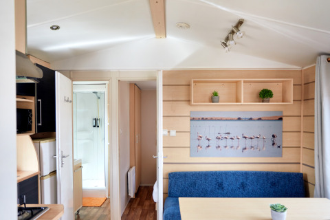 Interiør af Bungalow Confort Delta med køkken, spisebord, blå bænk, planter og et flamingobillede.