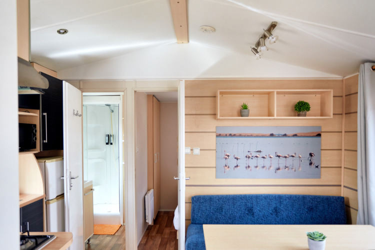 Interior del Bungalow Confort Delta con cocina, mesa de comedor, banco azul, plantas y foto de flamencos.