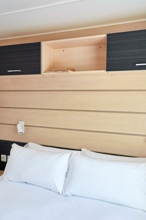 Interior photo of Bungalow Confort Delta, showing wood panels, white pillows on bed, and open cabinets.