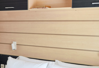 Interior photo of Bungalow Confort Delta, showing wood panels, white pillows on bed, and open cabinets.
