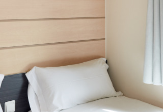 To enkeltsenge med hvide lagner og puder i en lys hytte på Bungalow Confort Delta, TAIGA Delta de l'Ebre, Spanien.