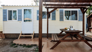 Terraza exterior con mesa y bancos de madera frente a una cabaña con contraventanas azules en Bungalow Essential Flamenc.