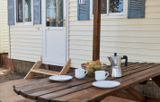 Udendørs spisebord foran Bungalow Essential Flamenc ved TAIGA Delta de l'Ebre i Spanien med kaffe og frugt.