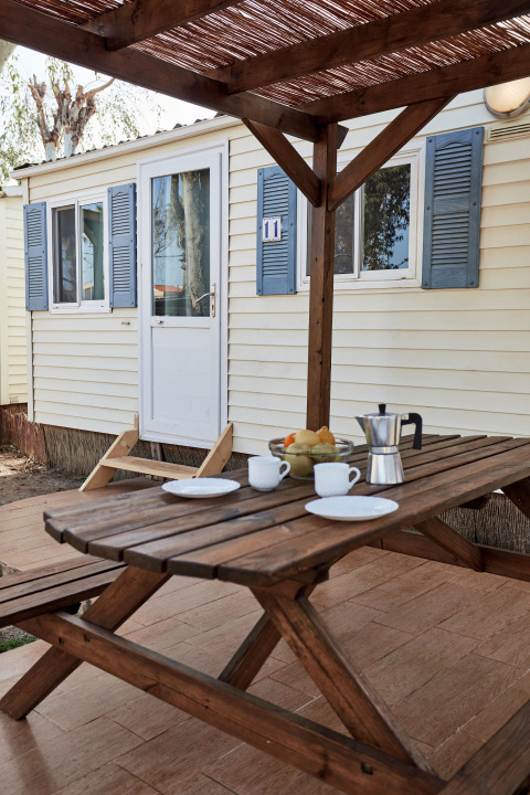 Holztisch vor dem Bungalow Essential Flamenc in TAIGA Delta de l'Ebre, Spanien, gedeckt mit Kaffee und Obst.