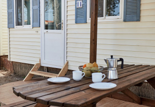 Holztisch vor dem Bungalow Essential Flamenc in TAIGA Delta de l'Ebre, Spanien, gedeckt mit Kaffee und Obst.