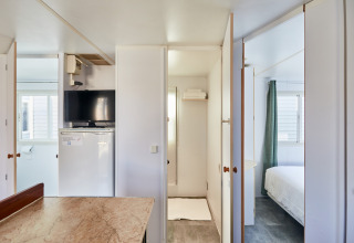 Interior de un bungalow luminoso con televisor, nevera pequeña, mesa y acceso a dormitorio y baño.
