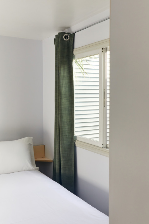 Habitación minimalista con cama blanca, cortina verde y ventana en Bungalow Essential Flamenc, TAIGA Delta de l'Ebre.