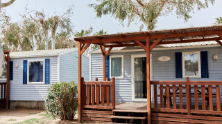 Vista exterior del Bungalow Confort Daurada con porche de madera, contraventanas azules y árboles al fondo.