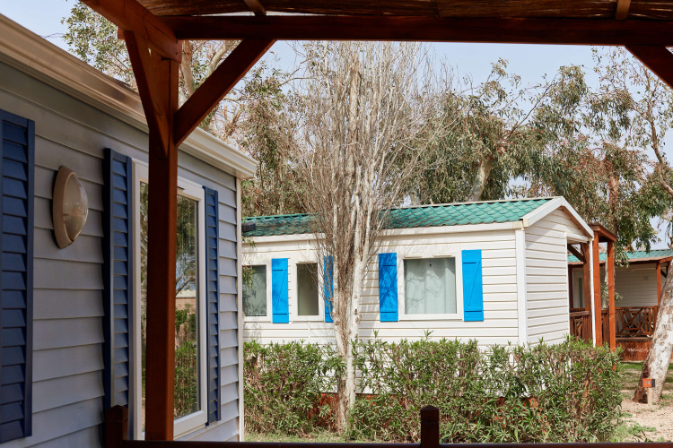 Bungalow Confort Daurada bij TAIGA Delta de l'Ebre in Spanje, witte huisjes met blauwe luiken en bomen.