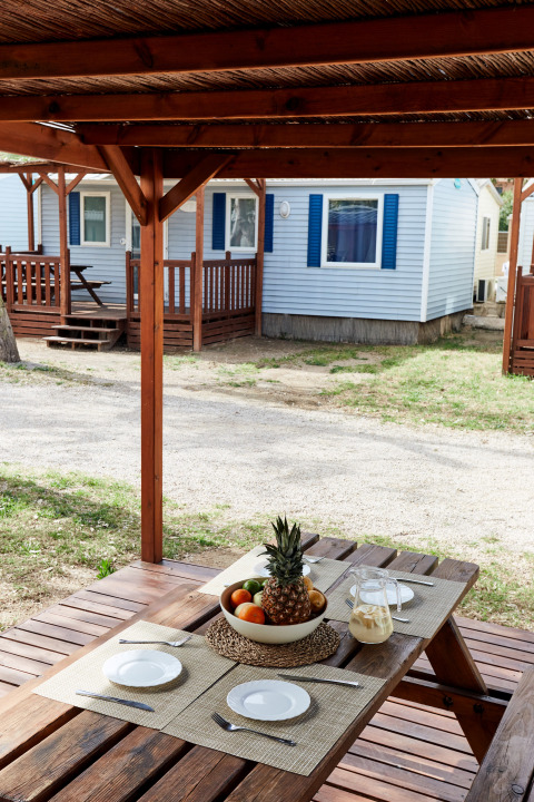 Buiten houten tafel onder overkapping bij Bungalow Confort Daurada, TAIGA Delta de l'Ebre, Spanje.