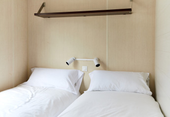 Habitación de cabaña moderna con dos camas individuales, sábanas blancas y lámparas en TAIGA Delta de l'Ebre, España.