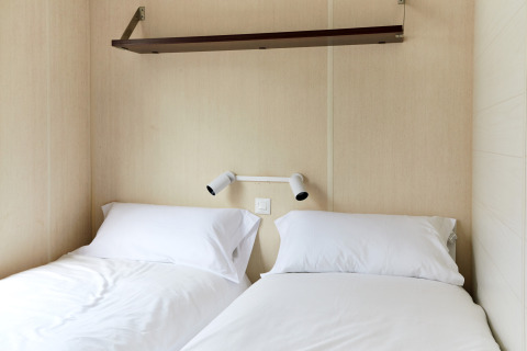 Moderne cabine met twee eenpersoonsbedden, witte lakens en wandlampjes bij TAIGA Delta de l'Ebre, Spanje.