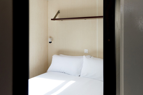 Kleine cabin met tweepersoonsbed, plank en lamp in Bungalow Confort Daurada, TAIGA Delta de l'Ebre, Spanje.