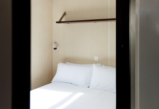 Kleine cabin met tweepersoonsbed, plank en lamp in Bungalow Confort Daurada, TAIGA Delta de l'Ebre, Spanje.