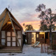 Glamping Cabin-Tent Senyoret ved solnedgang med træhytter, palmer og liggestole i et roligt udendørsmiljø.