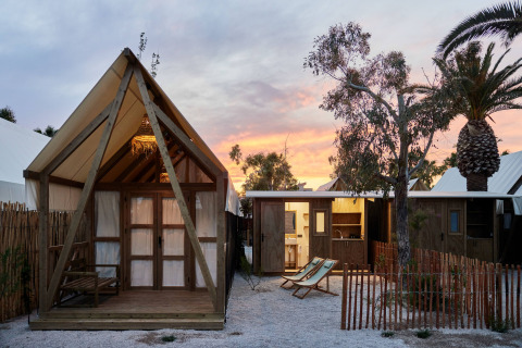 Glamping Cabin-Tent Senyoret al atardecer con cabañas modernas, palmeras y sillas reclinables al aire libre.