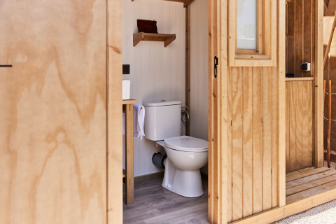 Vista interior de un baño de madera con inodoro y estante en una tienda glamping en España.