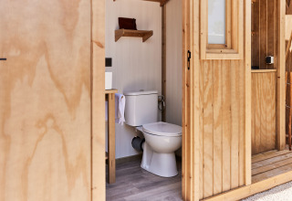 Binnenzicht van een houten badkamer met toilet en plank in een glamping tent in Spanje.