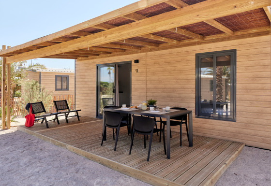 Außenbereich des Bungalow Premium Gregal mit überdachter Holzterrasse und Esstisch mit Stühlen.