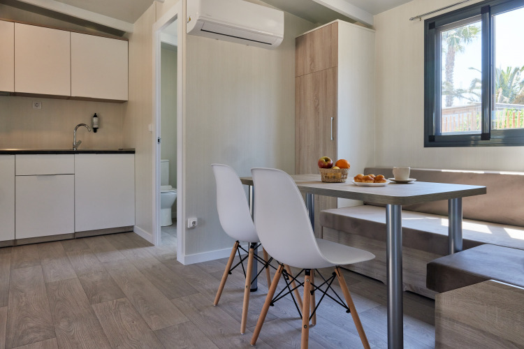 Modern glamping accommodation with kitchenette, dining area, and large window overlooking nature.