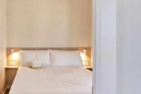 Camera da letto con letto matrimoniale, cuscini bianchi e libro aperto nel Bungalow Premium Gregal, TAIGA Delta de l'Ebre, Spagna.