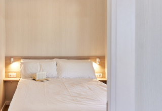 Schlafzimmer mit Doppelbett, weißen Kissen und offenem Buch im Bungalow Premium Gregal, TAIGA Delta de l'Ebre, Spanien.