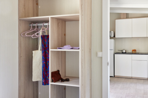 Alojamiento de glamping moderno con armario abierto, perchas y vista parcial de la cocina al fondo.